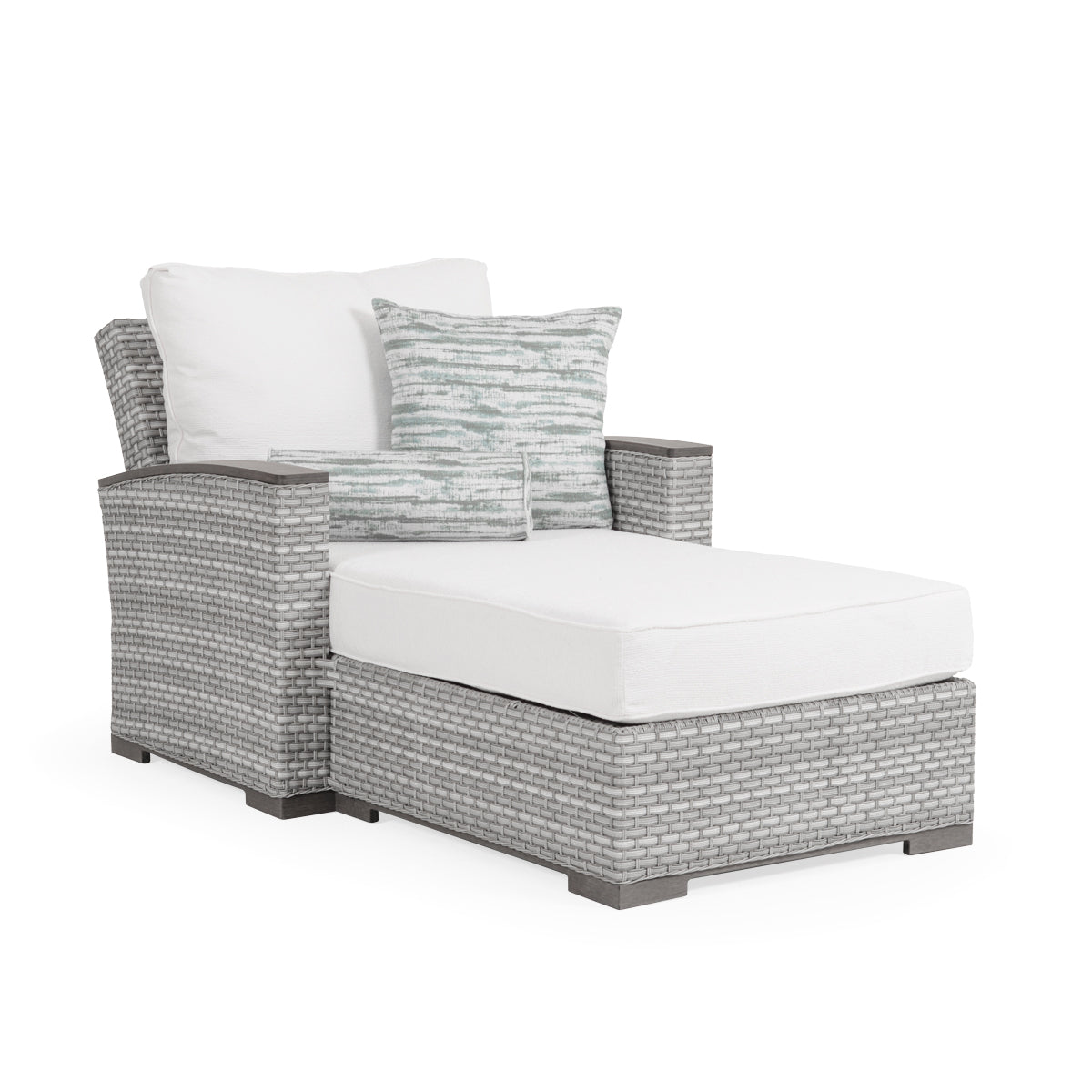 An outdoor wicker chaise and a half with a white cushion and a patterned pillow, set against a grey wicker background.